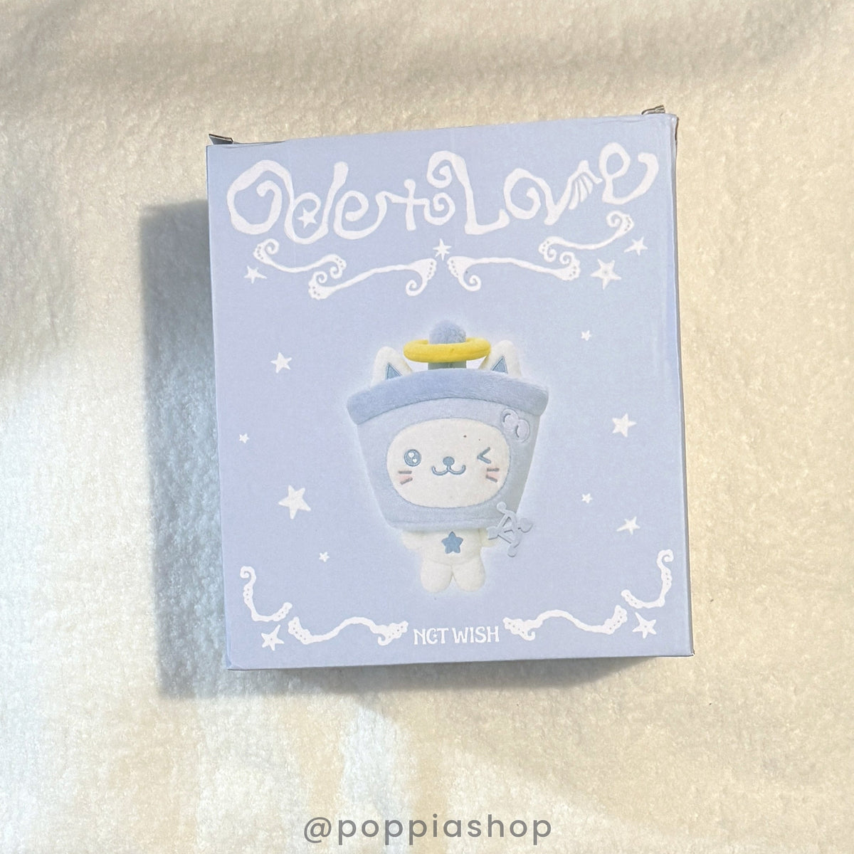 A square product box for an NCT WISH 'DeToLove' item, featuring a pastel lavender design with a cute cartoon character in a blue astronaut helmet. The box is photographed on a textured, light beige fabric background.