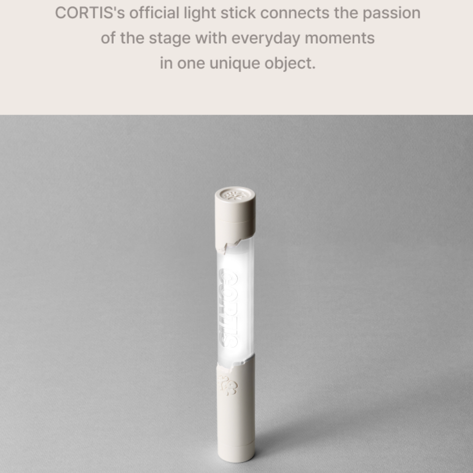 A tall cylindrical CORTIS light stick with a frosted white body and beige end caps, standing on a neutral gray surface. Text at the top reads, 'CORTIS's official light stick connects the passion of the stage with everyday moments in one unique object.